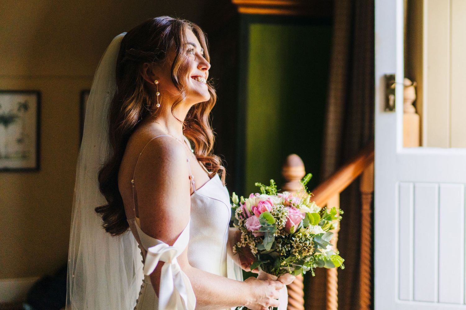 Bride in a white wedding dress laughs joyfully while holding a beautiful bouquet near a doorway. Castle Leslie Wedding Photographer Dublin
