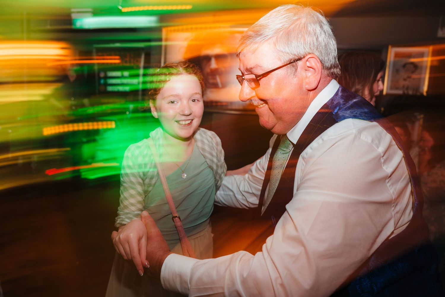 Motion-blur photograph with green and orange lights creating a festive dance party atmosphere.
