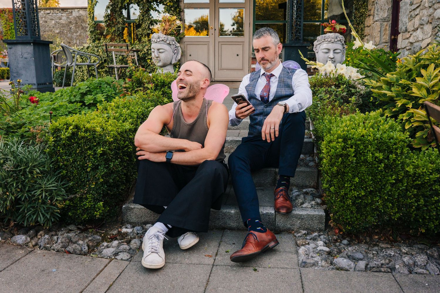 Garden setting with people relaxing on stone walls surrounded by lush greenery. . Village Barn Tyrrellspass wedding photographer Ireland