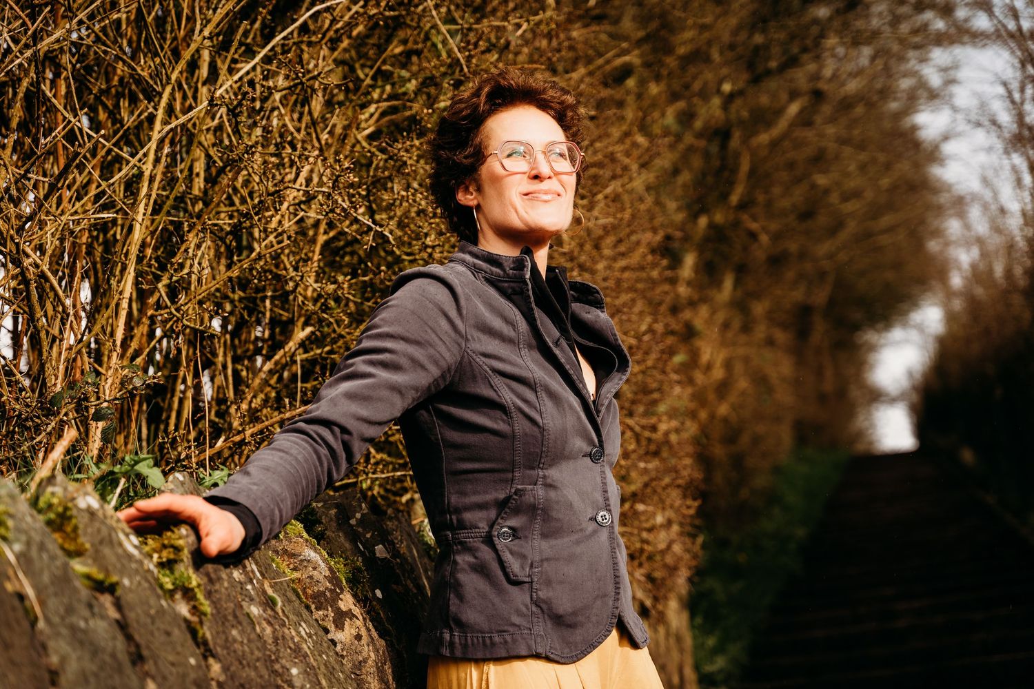 Figure in dark clothing performs expressive dance movements along a wooded path at golden hour. Portrait PHOTOGRAPHER Dublin