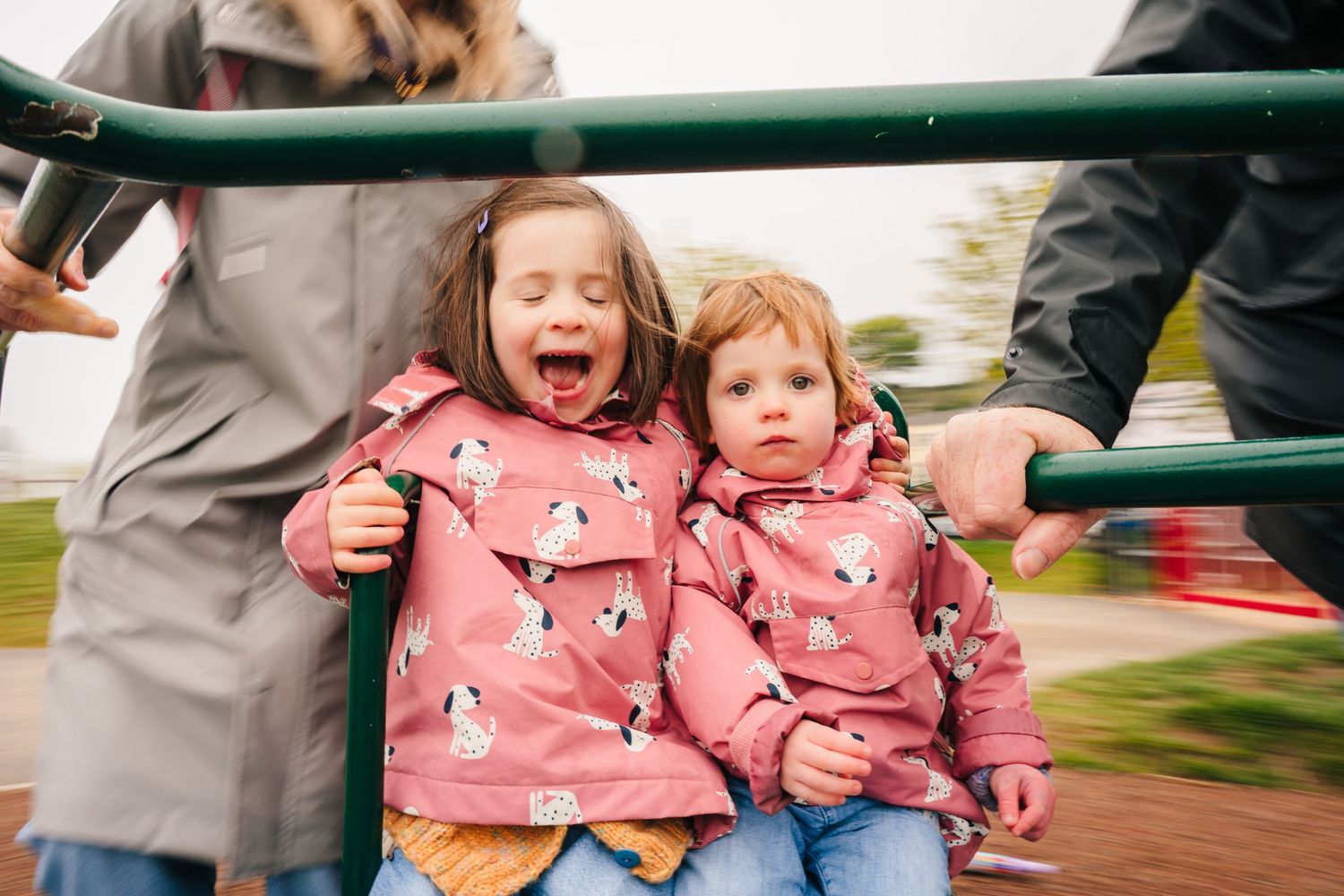 Two children in matching pink patterned sweatshirts riding on playground equipment with motion blur in the background. PHOTOGRAPHER Dublin