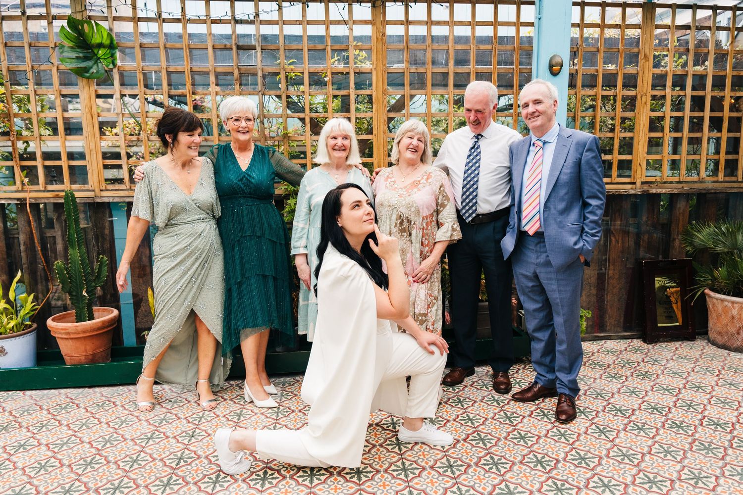 A group poses together on an outdoor patio with wooden lattice and potted plants in the background. House Dublin Wedding Photographer