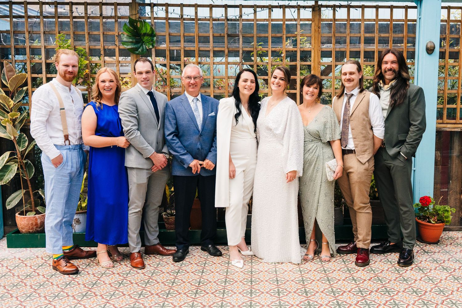 A wedding party poses together on a patio with a lattice backdrop and potted plants. House Dublin Wedding Photographer