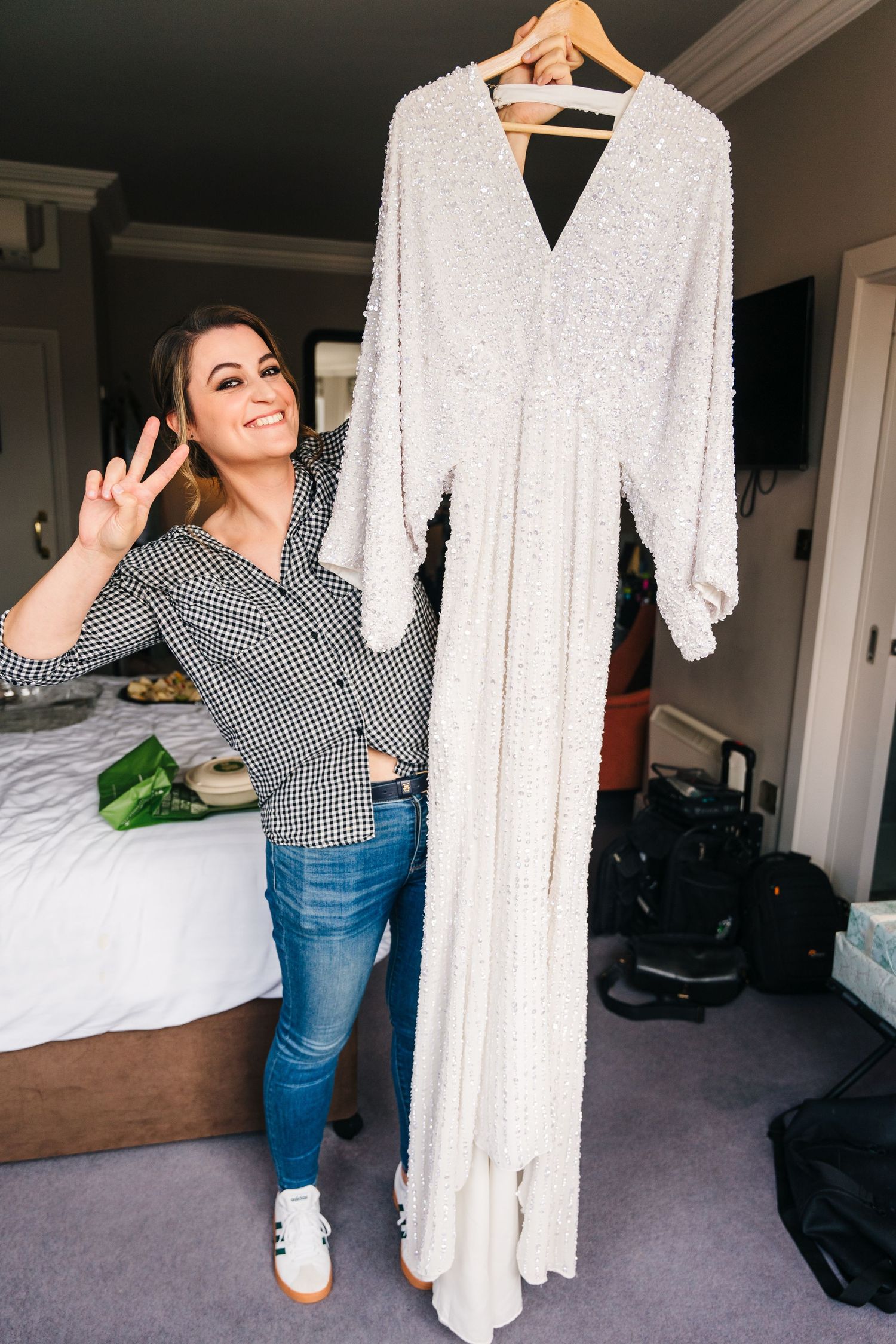 A white sequined wedding gown hangs on display while someone in a checkered shirt and jeans gestures excitedly. House Dublin Wedding Photogr