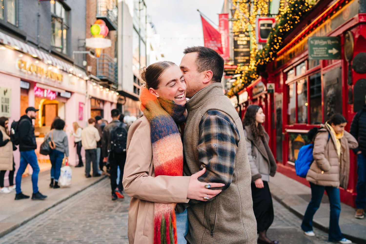 A couple shares a romantic moment on a charming cobblestone street lined with festive pub decorations in Dublin. PHOTOGRAPHER Dublin
