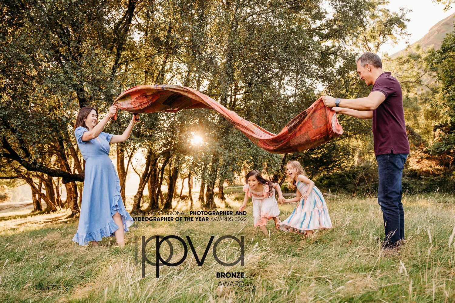 Family playing with flowing fabric in golden sunlit field with trees. Family PHOTOGRAPHER Dublin PHOTOGRAPHER Dublin