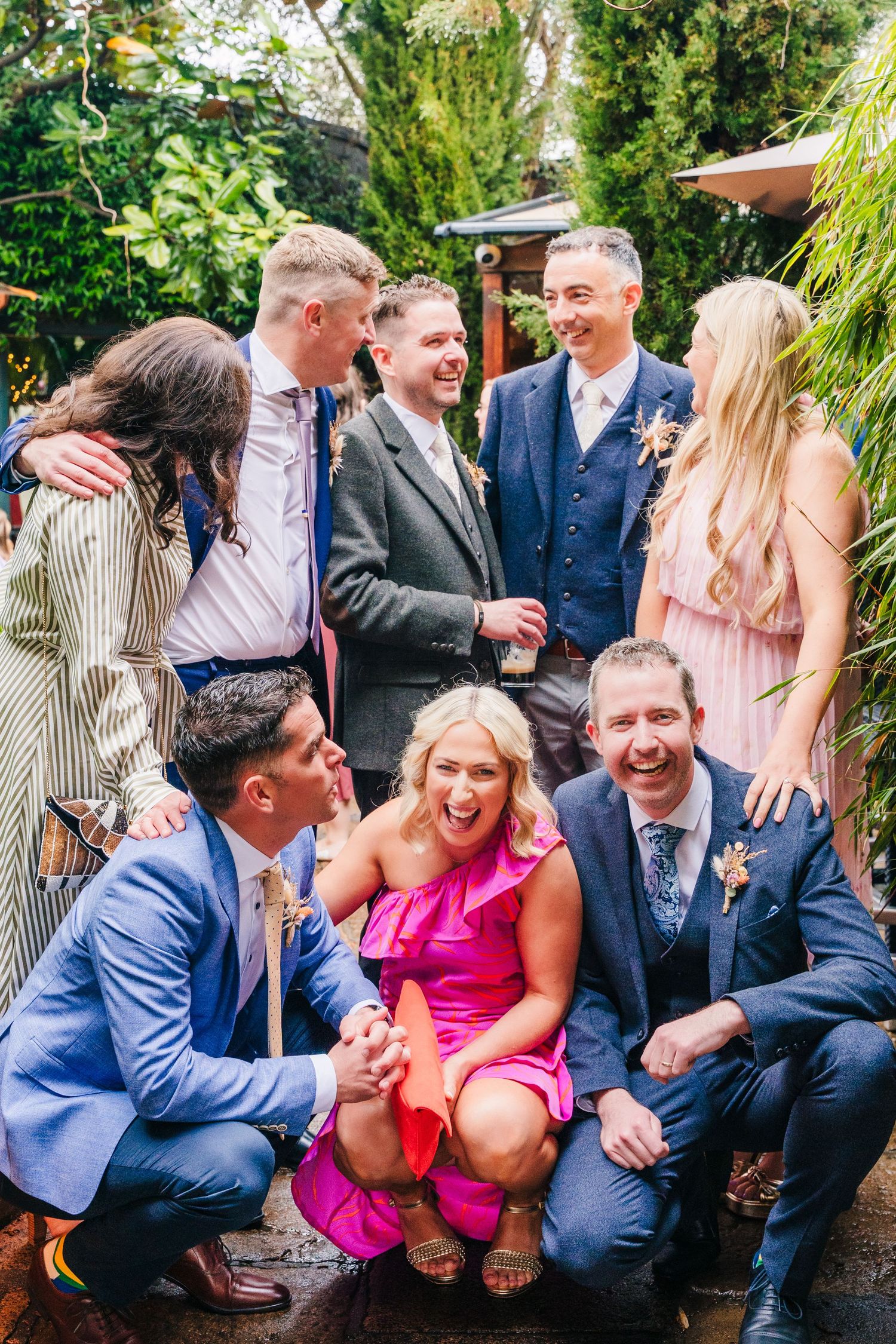 Wedding party members in formal attire sharing laughs in a lush garden setting. Marco Pierre Dublin Wedding Photographer