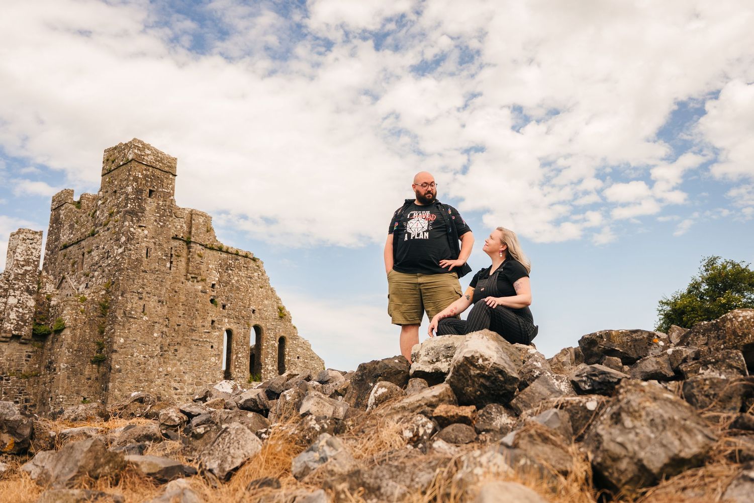 Couple standing on rocky outcrop near ancient stone church ruins against cloudy blue sky in Ireland. PHOTOGRAPHER Dublin ireland