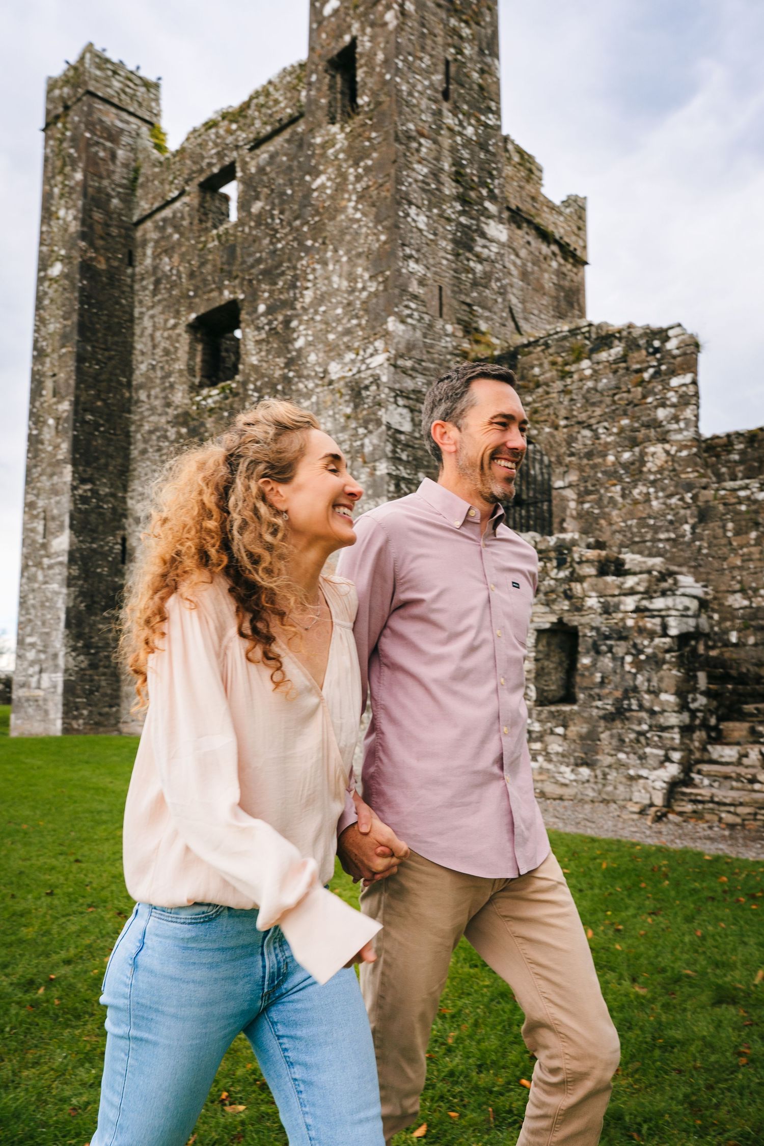 Couple laughing and embracing near ancient stone castle ruins on a grassy hill. BEctive abbey family photographer dublin