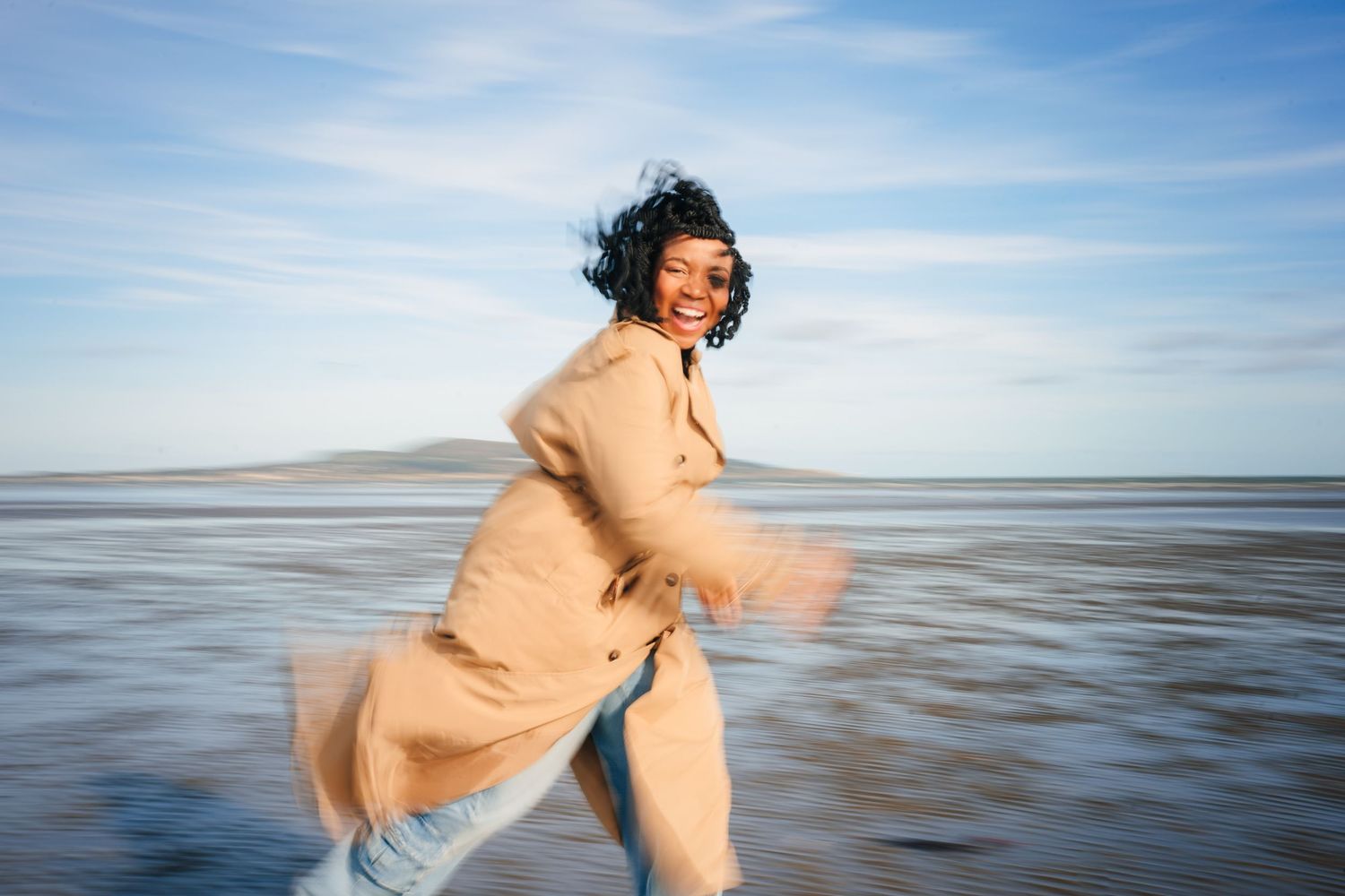 Figure dances freely on sandy beach against blue sky and calm ocean waters. Dublin professional headshot photographer