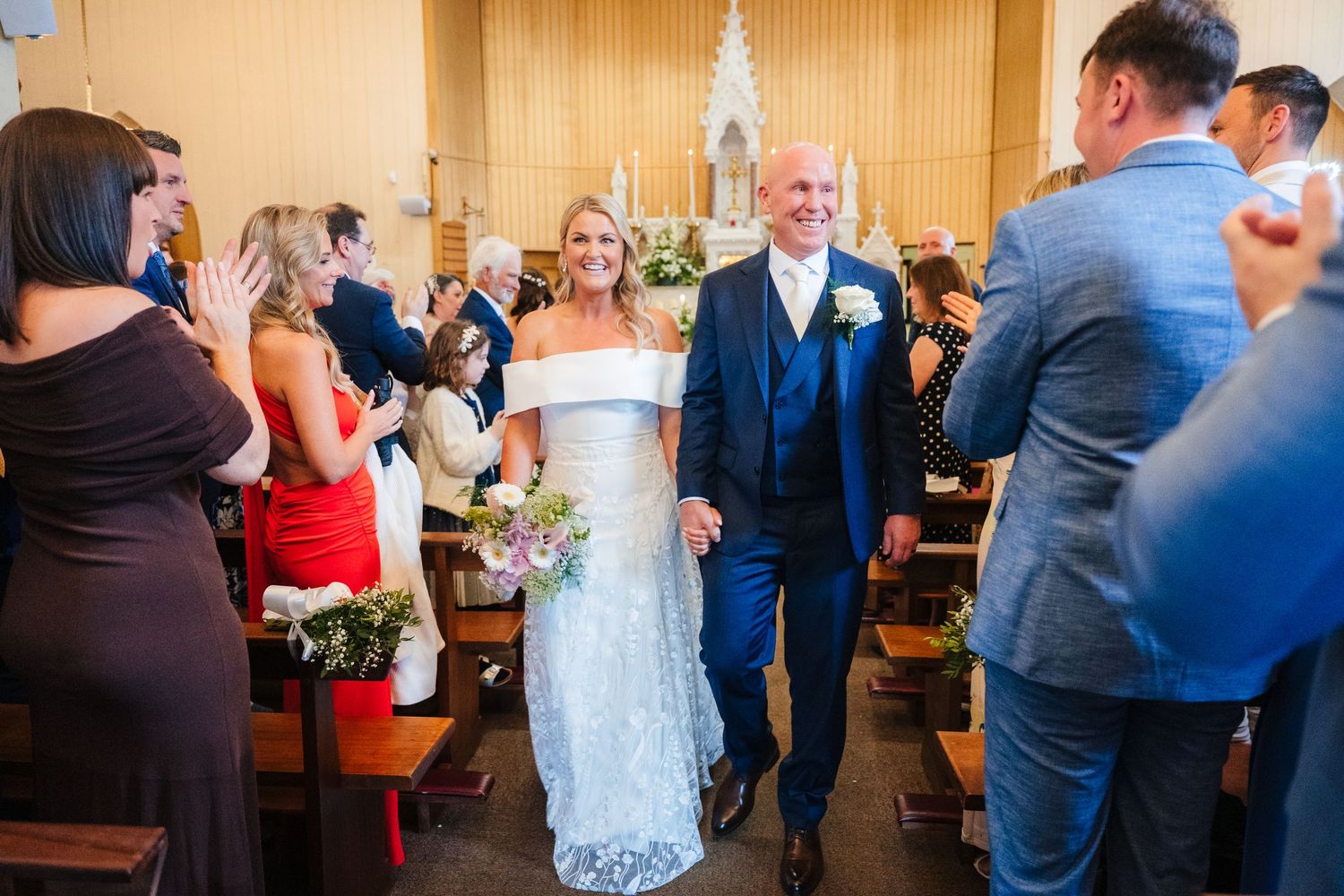 Wedding ceremony in a bright venue with the couple walking down the aisle surrounded by guests. The Dean Dublin Wedding Photographer