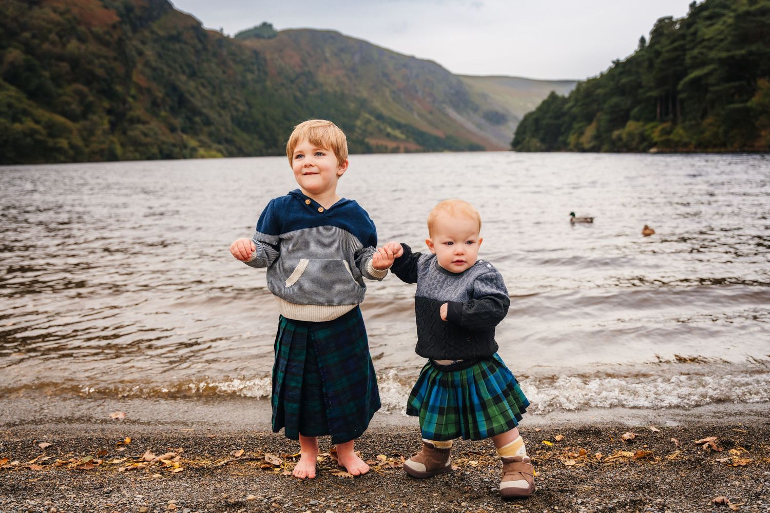 Children play together on a rocky beach shoreline with mountains and a lake in the background.Family photogrAPHER DUBLIN
