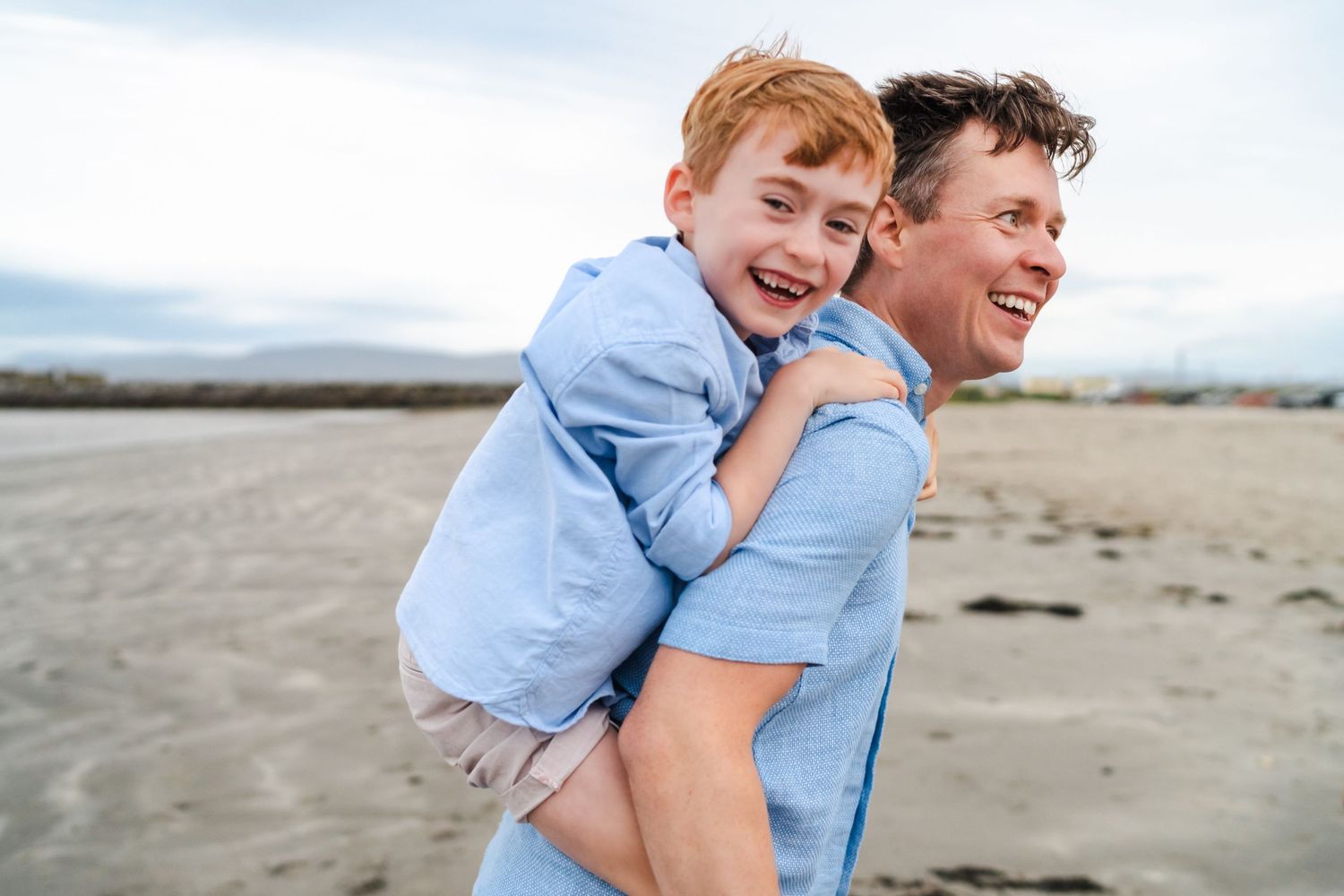 A joyful family moment captured at the beach with everyone wearing coordinating light blue and white outfits.  Family photographer Dublin Ir