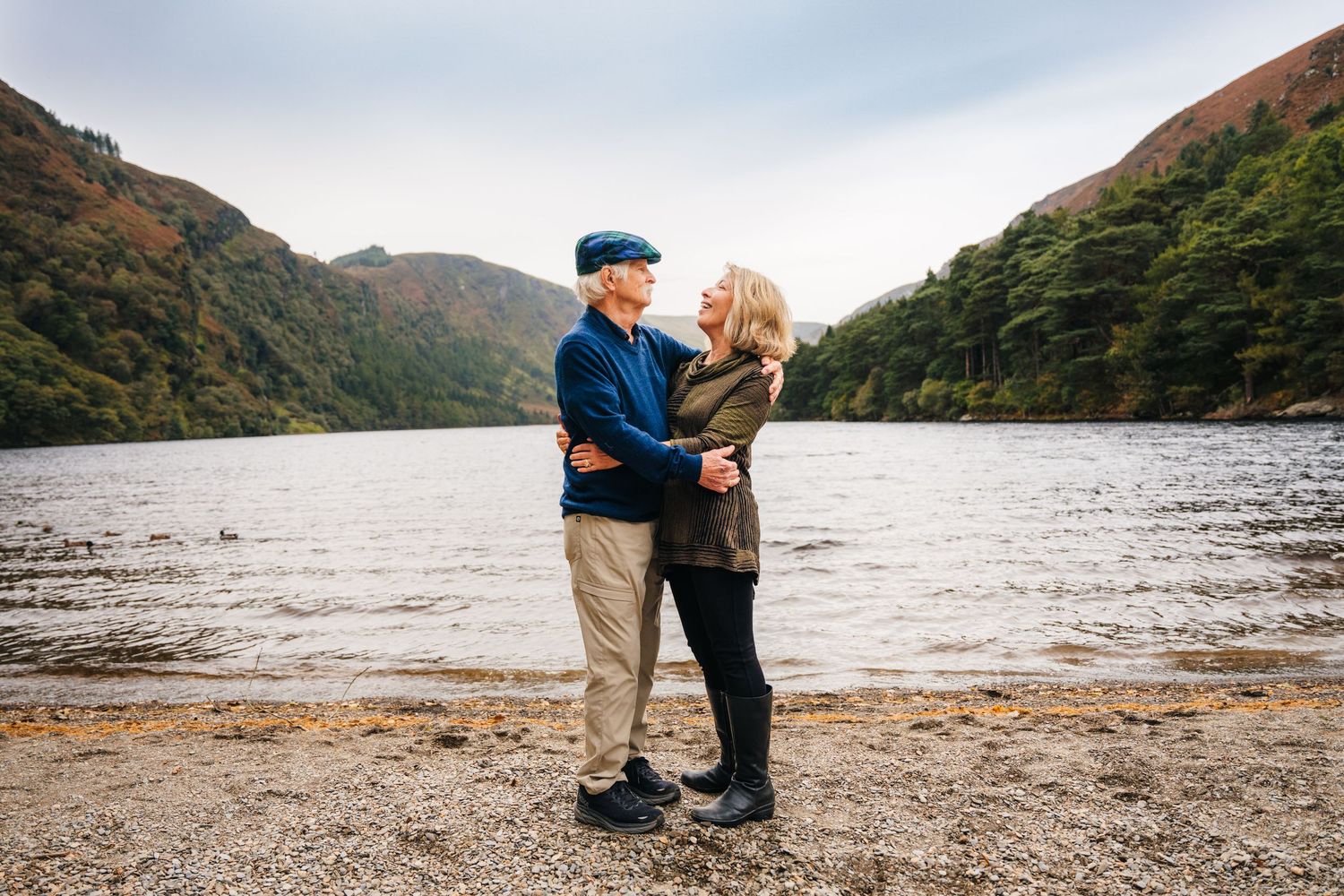 A couple enjoys a romantic moment along a scenic lakeside with mountains in the background during autumn.Family photogrAPHER DUBLIN