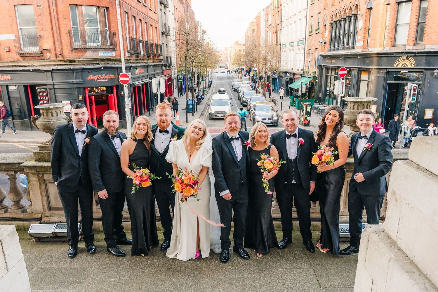 Wedding party group stands together on an urban street with brick buildings in the background. City Hall Dublin Photographer
