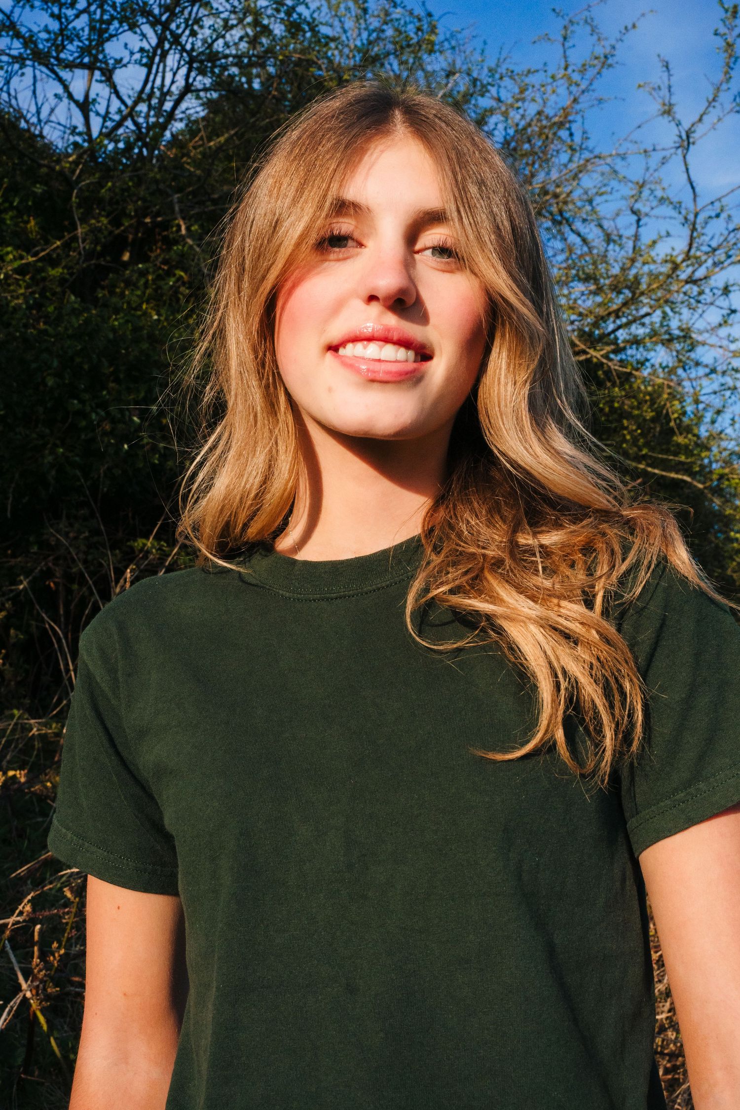 A person with long blonde hair wearing a green t-shirt smiles warmly in natural sunlight. Photographer Ireland dublin