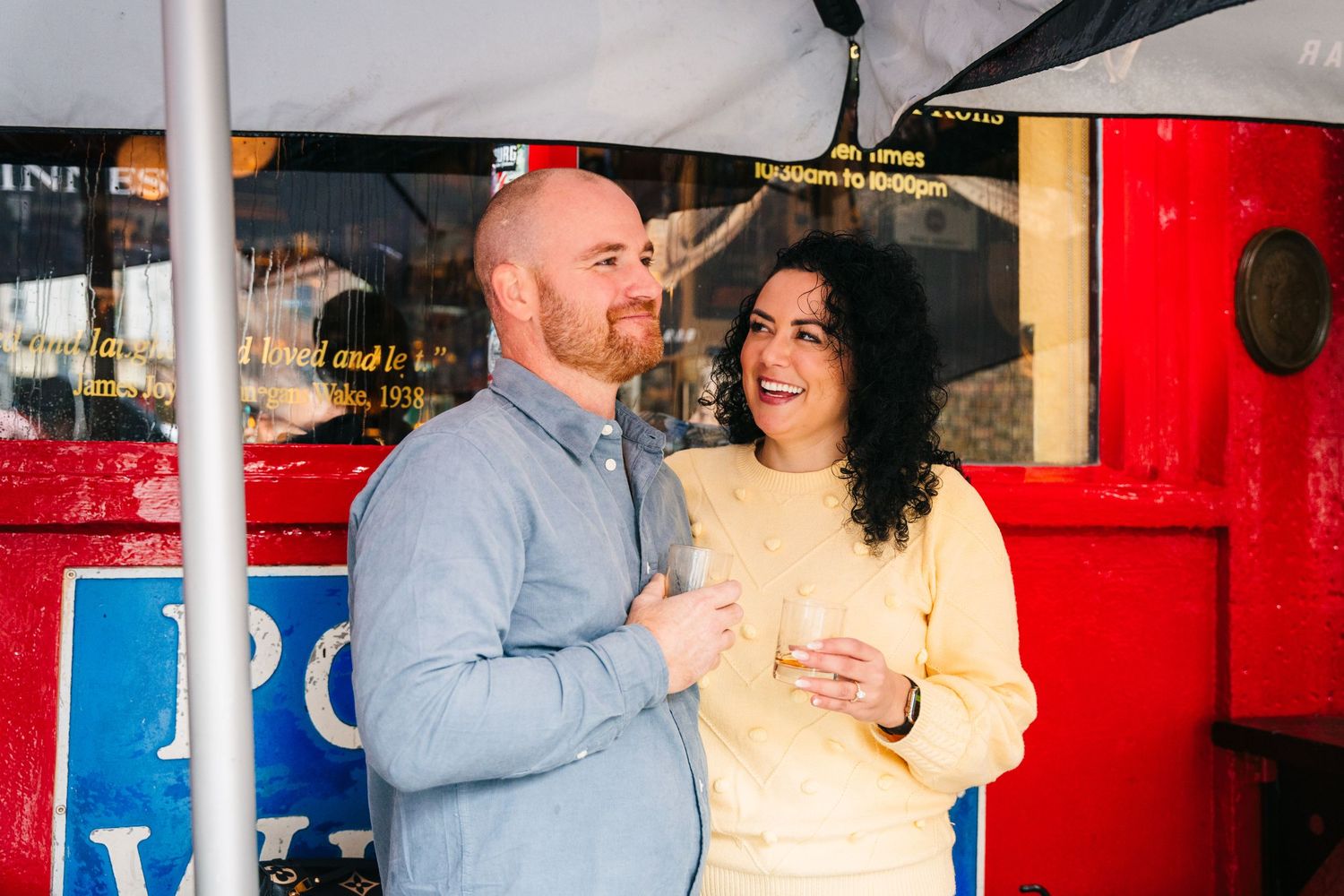 People laughing together during a candid social gathering in front of brightly colored storefront signage. Proposal Dublin Photographer