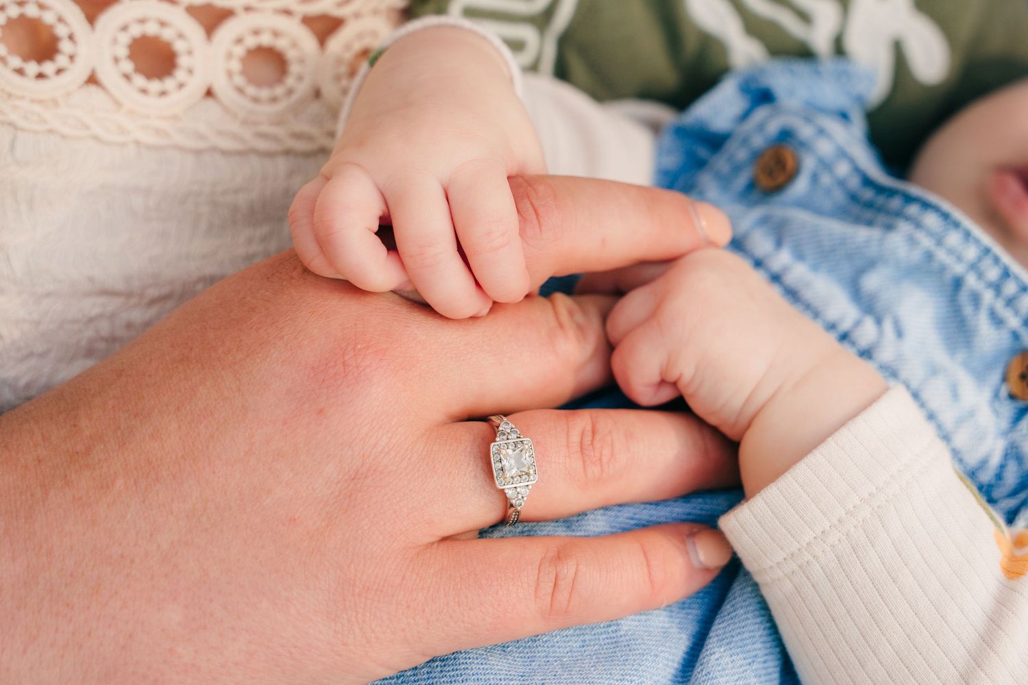 A tiny baby hand gently holds an adult hand wearing a sparkling engagement ring. Family PHOTOGRAPHER Dublin