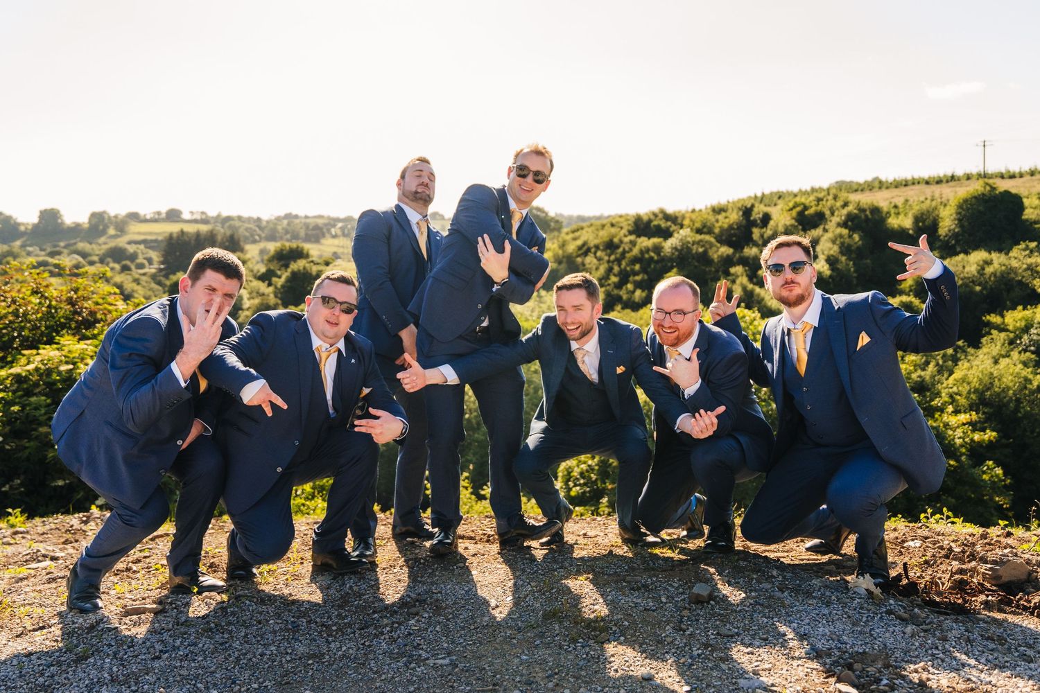 Poulaphouca Wedding photographer wicklow  Groomsmen in navy suits striking playful poses together on hilltop at sunset.