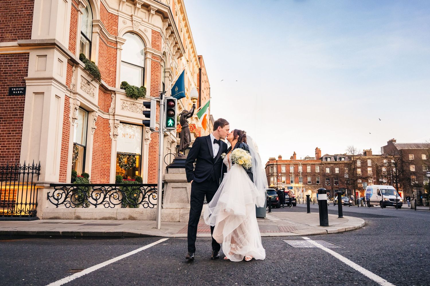 A wedding party walks along a sunny urban street with historic brick buildings. Wedding PHOTOGRAPHER Dublin