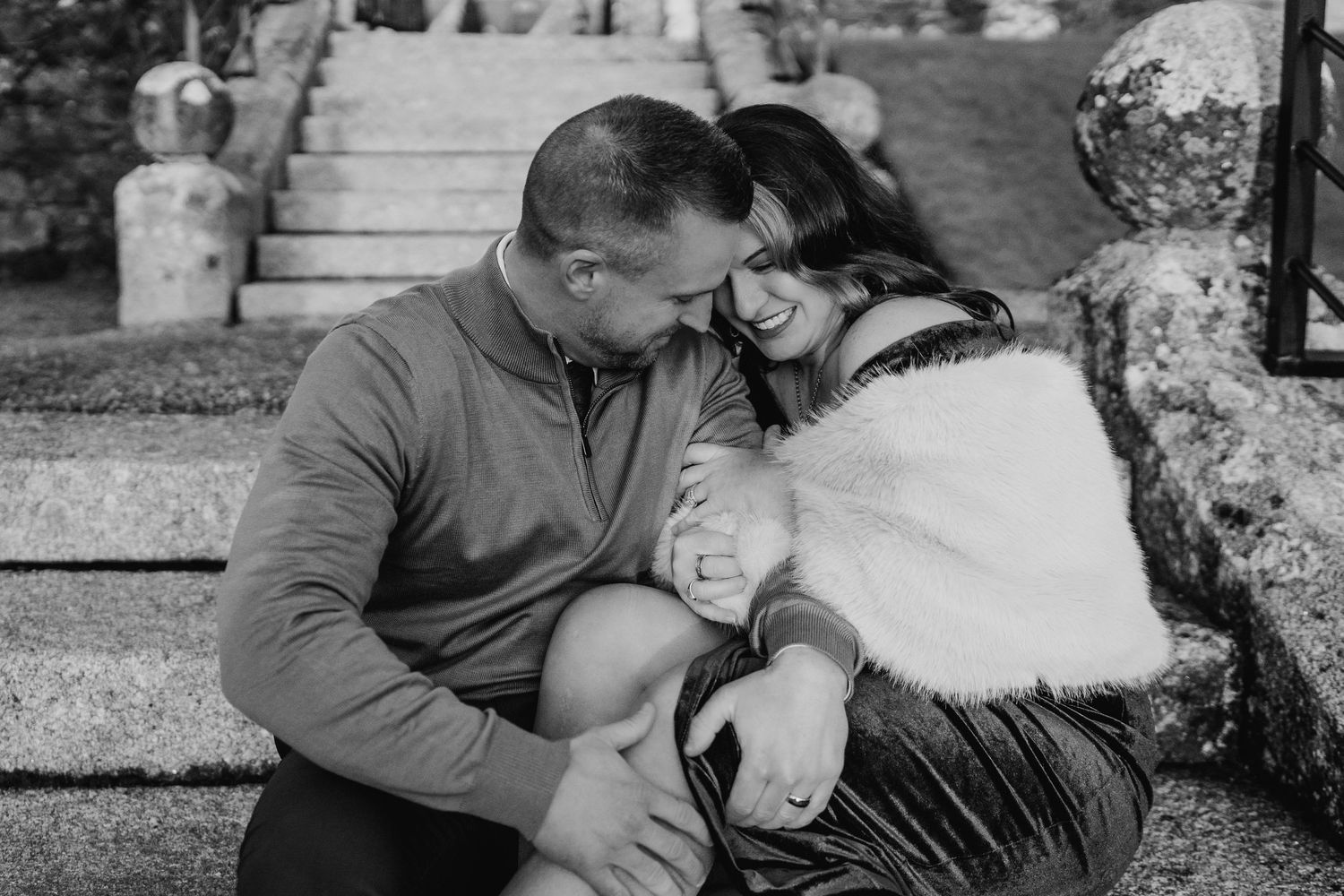 A couple sits close together on stone steps sharing an intimate moment in black and white. PHOTOGRAPHER Dublin ireland