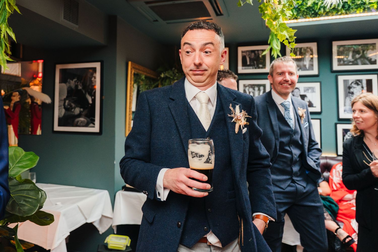 Candid moments of wedding guests mingling in a venue decorated with hanging plants and photographs.