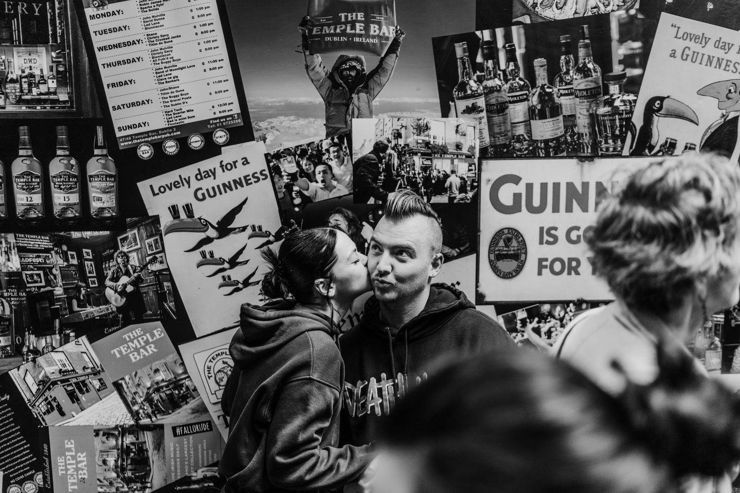 Black and white photograph of a crowded pub interior with Guinness advertising posters on the walls. PHOTOGRAPHER Dublin ireland