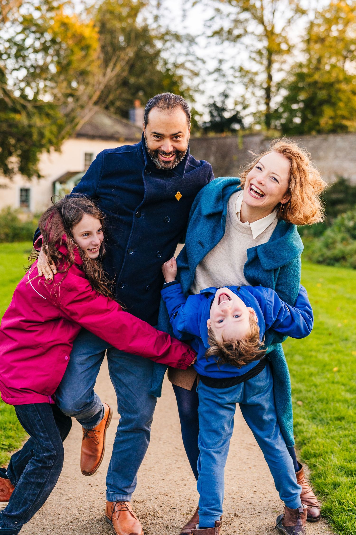 Family members share joyful embraces and laughter while walking together on an autumn path surrounded by trees. family PHOTOGRAPHER Dublin