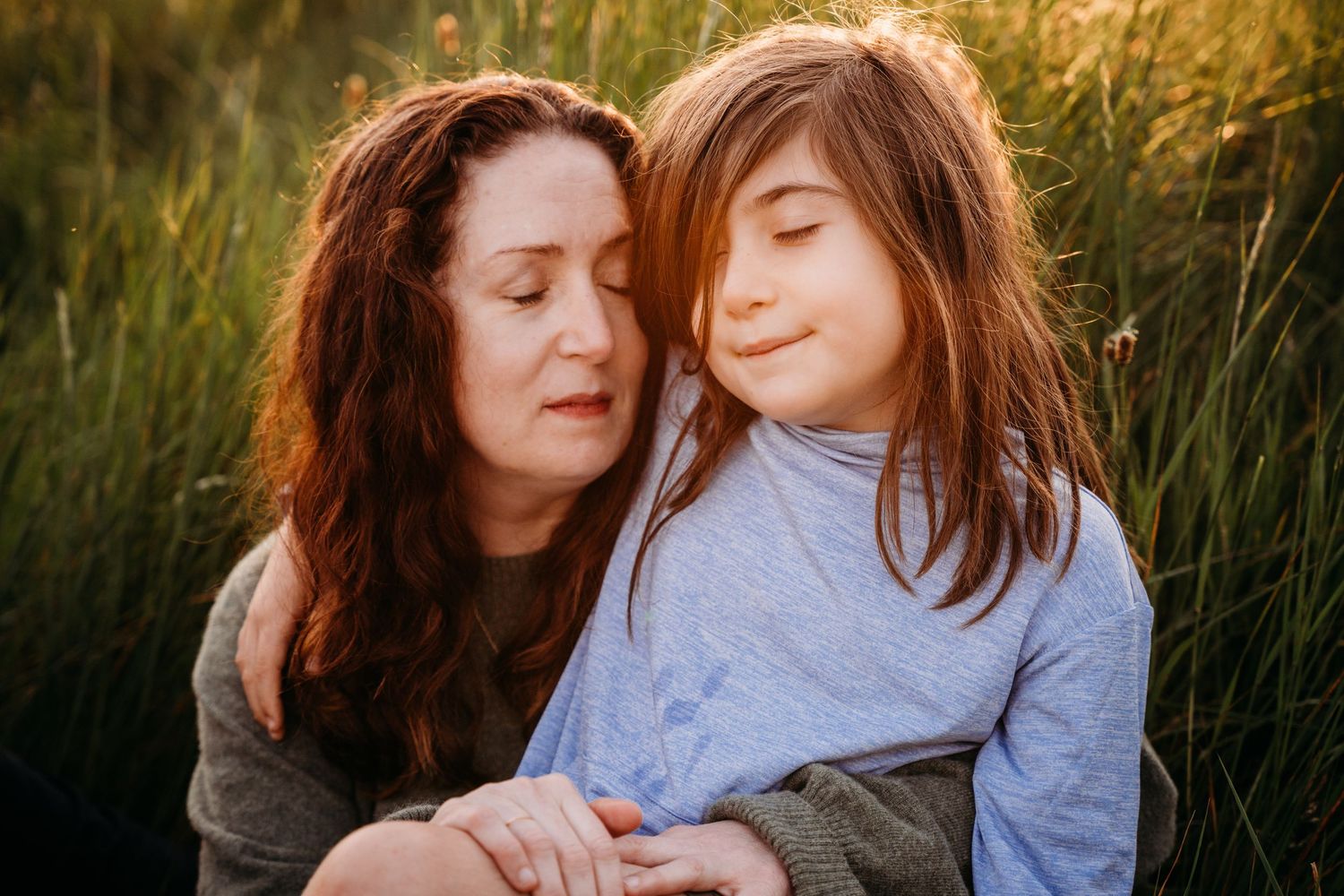 Two people share tender moment together in golden sunlit field of tall grass. family PHOTOGRAPHER Dublin