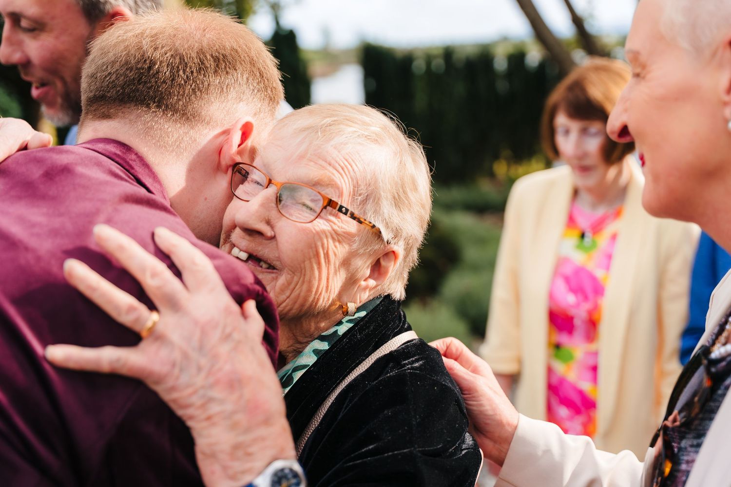 Emotional embrace at outdoor wedding celebration with guests in background. LGBTQ Ashley Park Wedding Photographer
