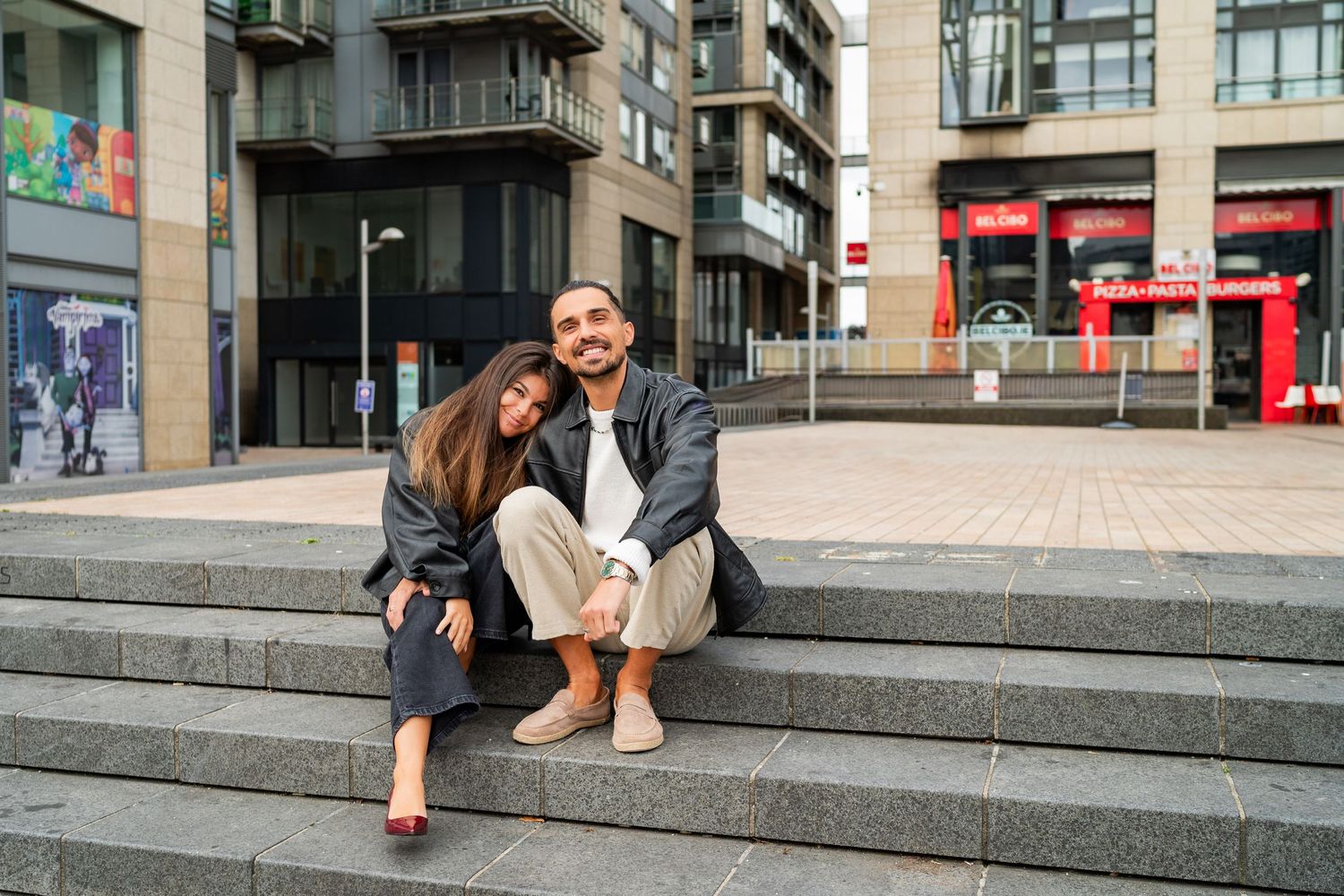 Group sitting on urban steps chatting and using mobile phones in front of modern city buildings. Couple's Photoshoot PHOTOGRAPHER Dublin