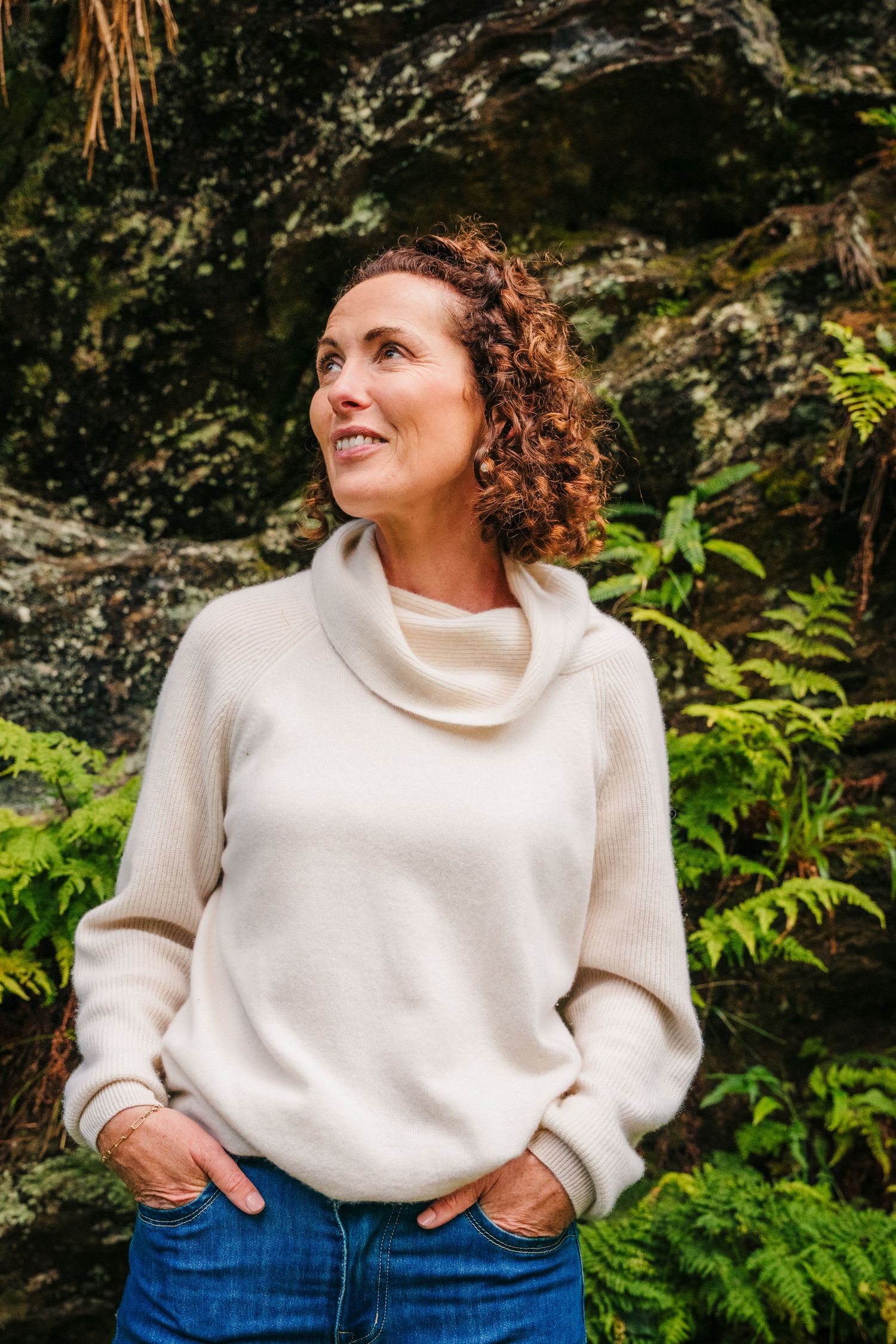Family photographer Ireland Dublin Woman in white sweater and jeans poses against natural rock formations.