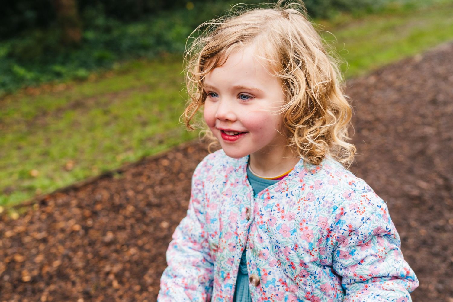 Family photographer Dublin Ireland  Young child smiling with rosy cheeks and curly blonde hair wearing a floral print coat outdoors.