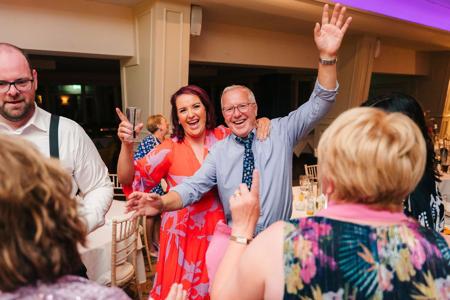 Wedding reception guests dancing and celebrating with raised arms in colorful outfits. Portmarnock Hotel Wedding PHOTOGRAPHER Dublin
