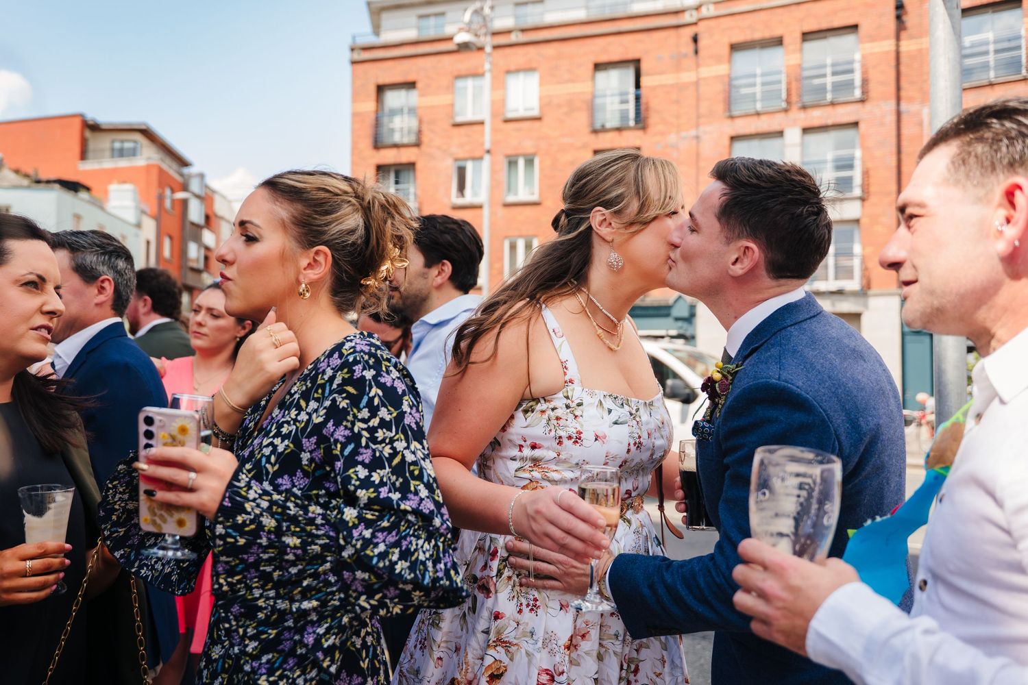 Wedding guests laugh and celebrate together during an outdoor reception in front of a brick building. Same sex wedding PHOTOGRAPHER Dublin