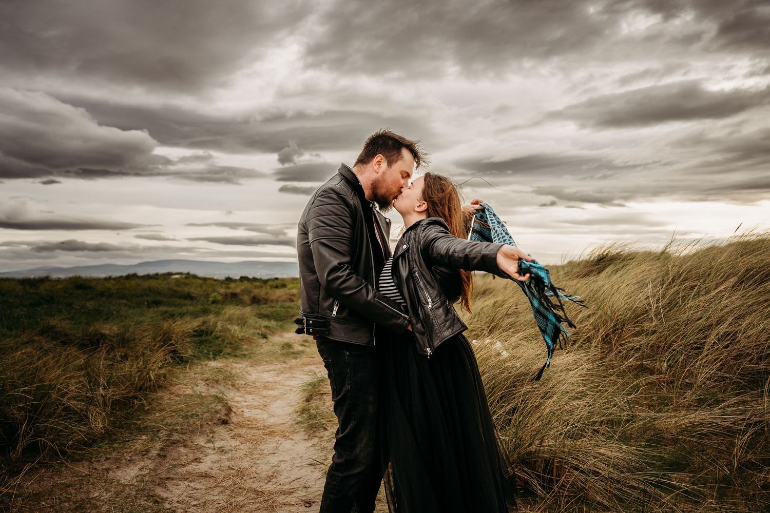 Dramatic coastal scene with stormy clouds and two figures in dark clothing on a windswept beach path. engagement PHOTOGRAPHER Dublin