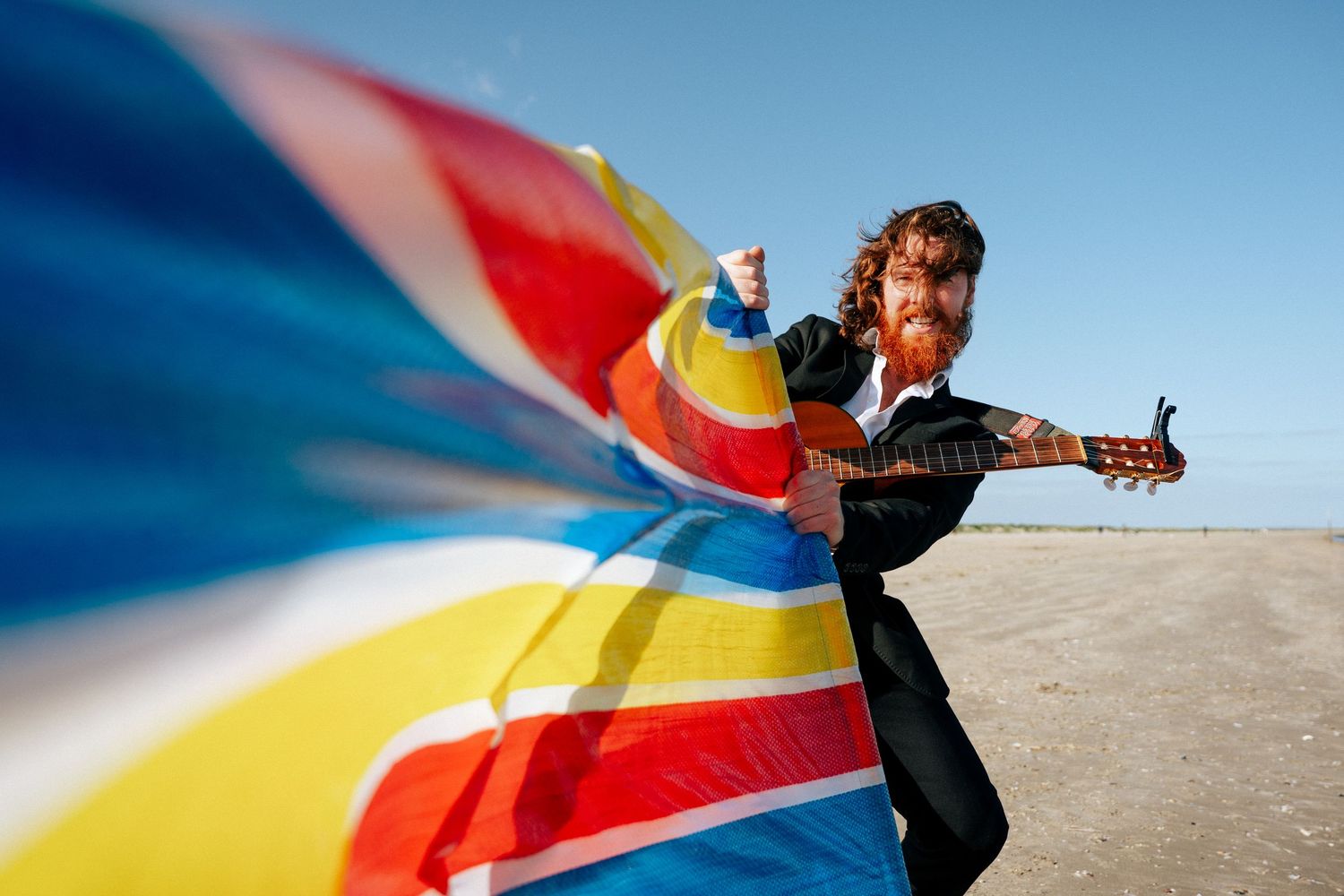 Colorful fabric billows in the wind as someone poses with thumbs up against clear blue sky on sandy beach. PHOTOGRAPHER Dublin