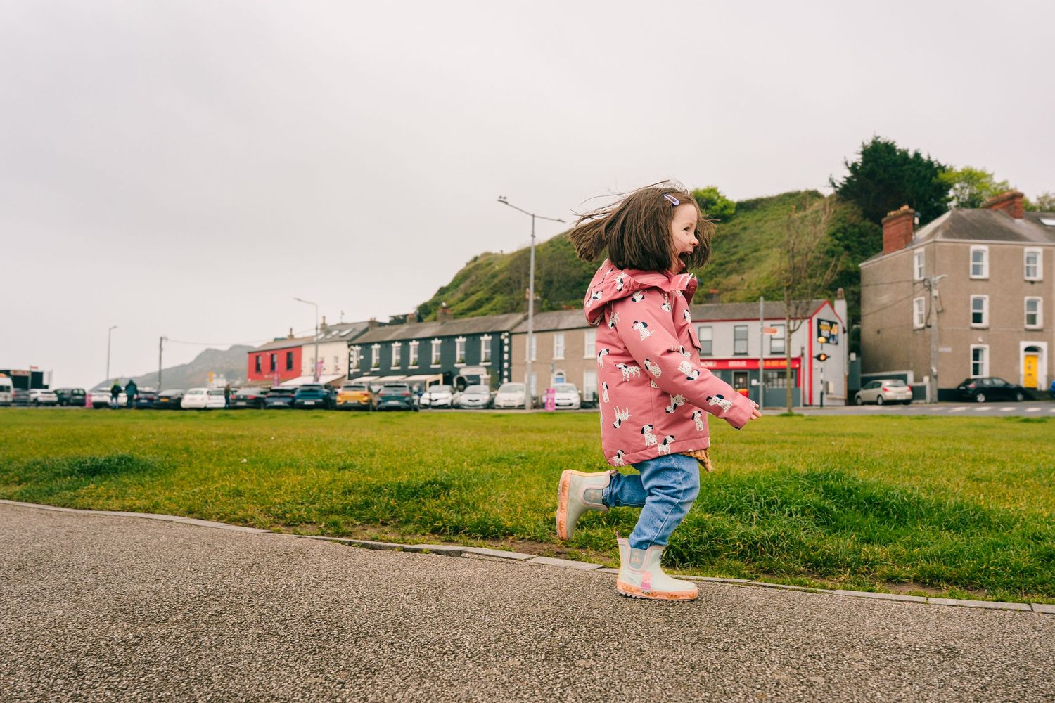 A pink toy wagon sits on a paved path near the grass while children play outdoors. PHOTOGRAPHER Dublin
