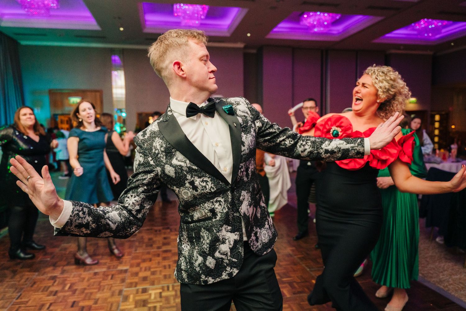 Energetic dance floor moments captured at wedding reception with purple ambient lighting.  Wedding PHOTOGRAPHER Trim Castle