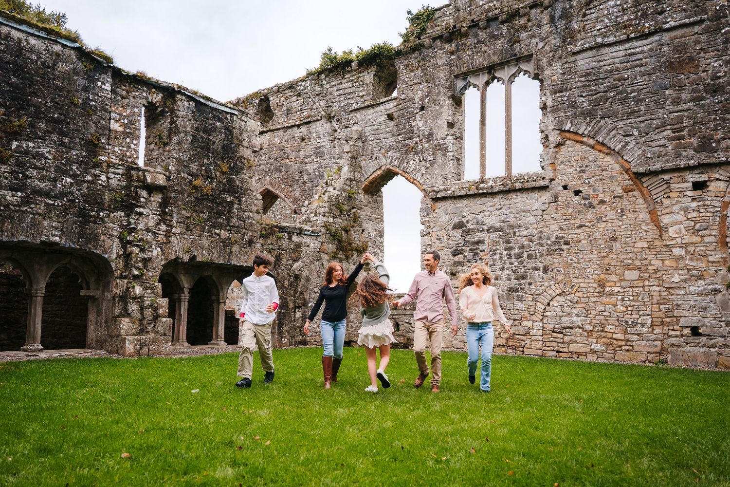 People stroll through ancient stone castle ruins with arched windows and weathered walls. BEctive abbey family photographer dublin