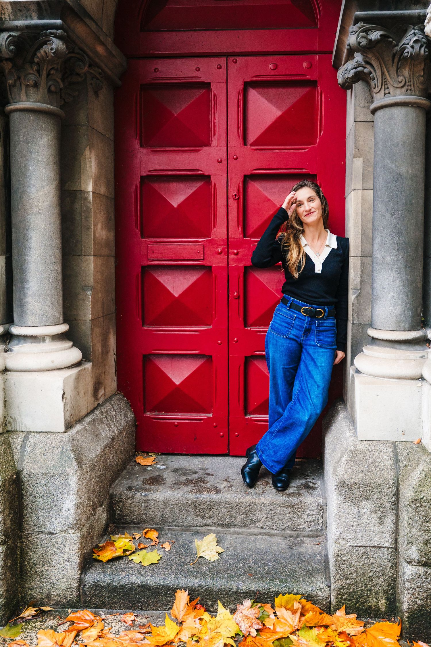 Autumn fashion photo with model posing against large red door with fallen leaves. professional headshots dublin photographer