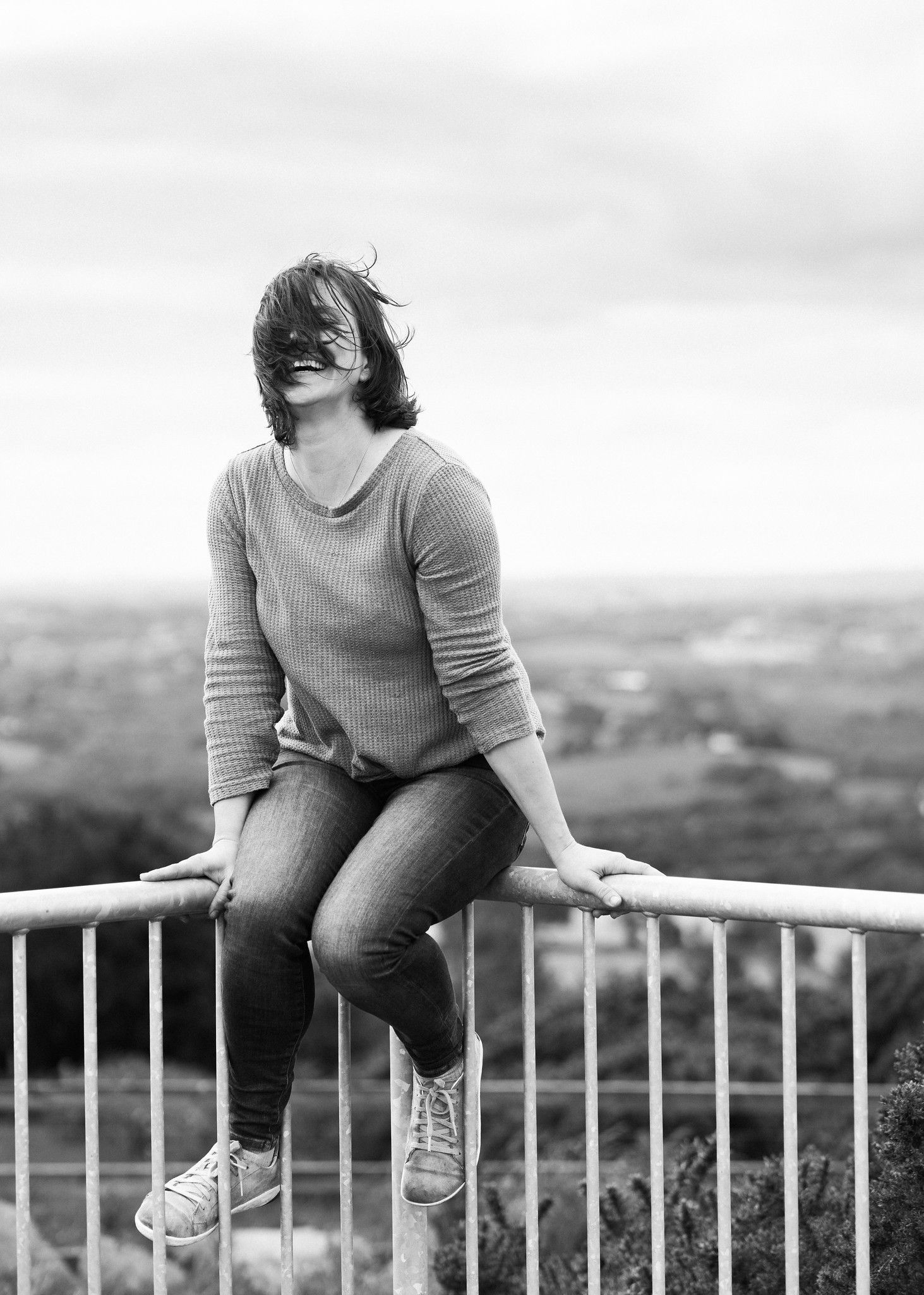 A grayscale photograph shows a person in casual attire sitting on a railing overlooking a distant landscape. PHOTOGRAPHER Dublin ireland