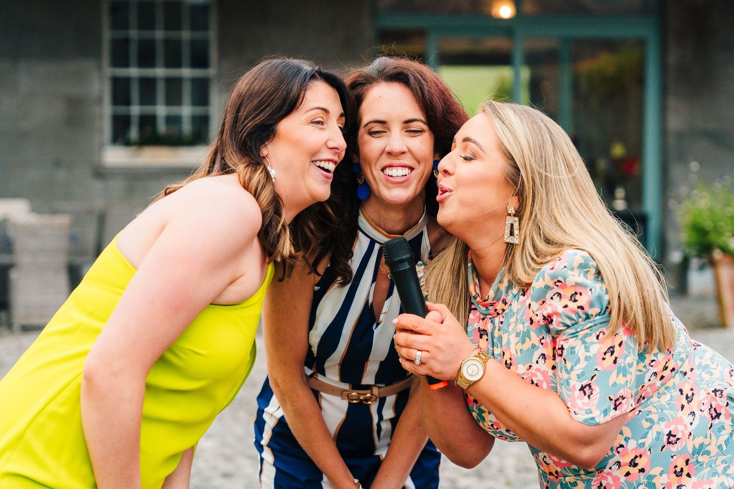 Three joyful friends laughing together outdoors in colorful summer outfits while sharing a fun moment. Wedding PHOTOGRAPHER Dublin