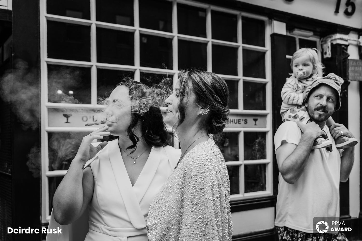 A candid black and white moment captures wedding guests sharing laughter outside a venue. PHOTOGRAPHER Dublin Wedding Photographer Dublin Ir