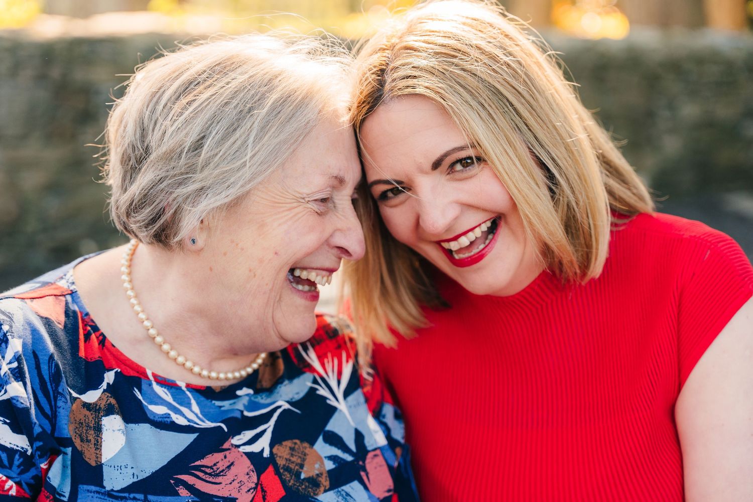 Two generations share a candid moment of joy and laughter while embracing and wearing red and blue outfits. family PHOTOGRAPHER Dublin