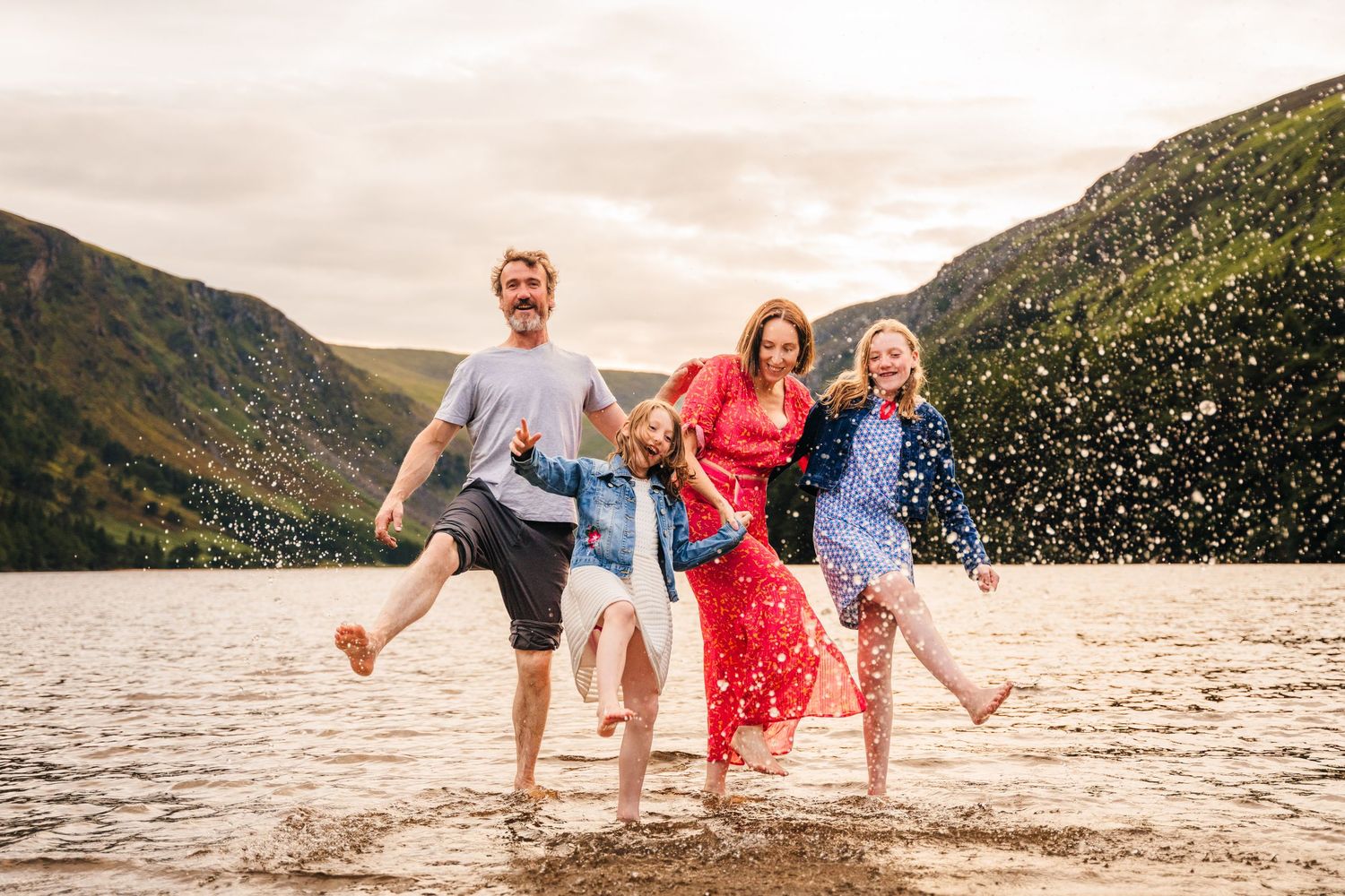 Group plays and splashes together at the edge of a scenic mountain lake during sunset. family PHOTOGRAPHER Dublin