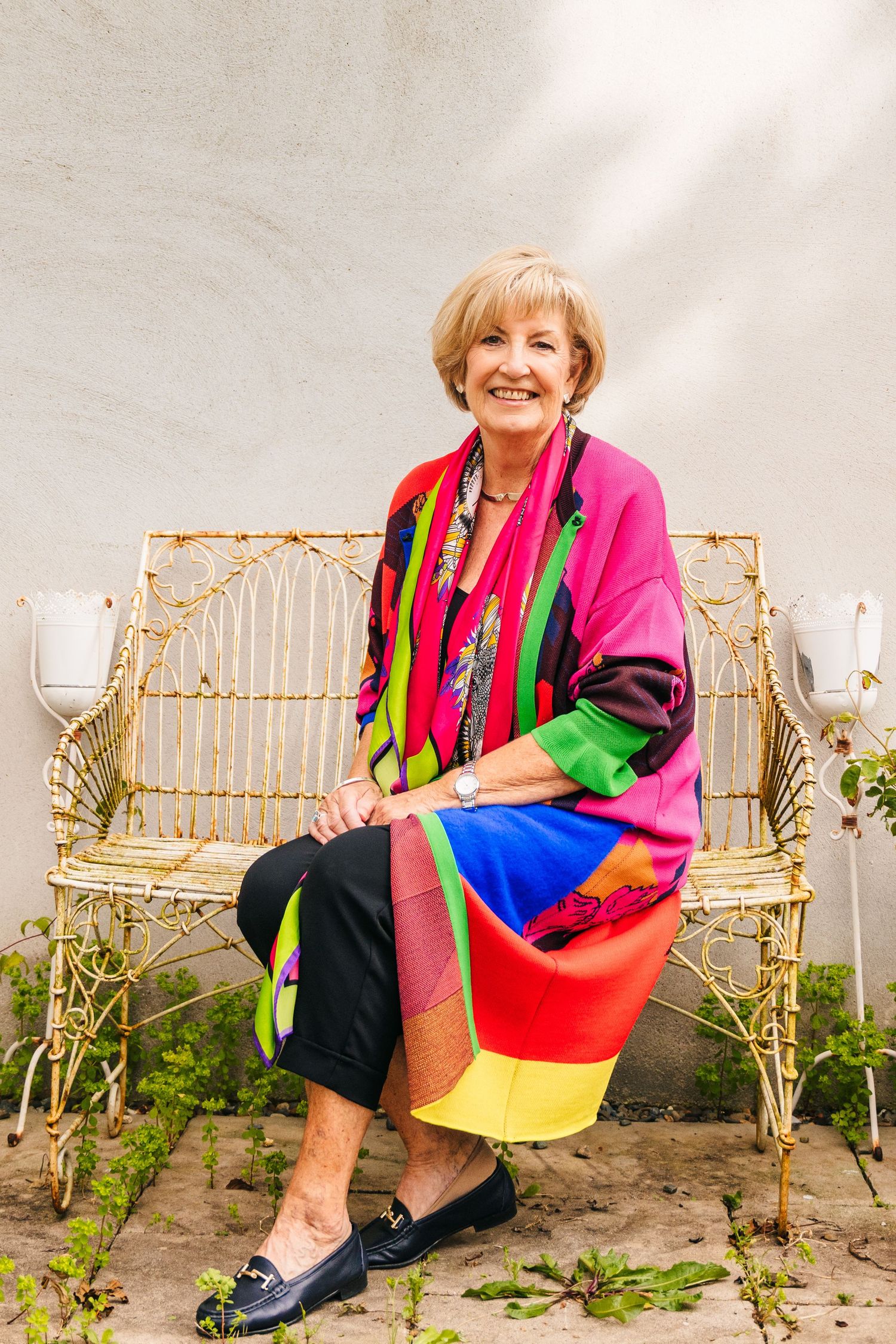 A person wearing colorful clothing sits on a wicker bench in a garden setting. Professional headshots PHOTOGRAPHER Dublin