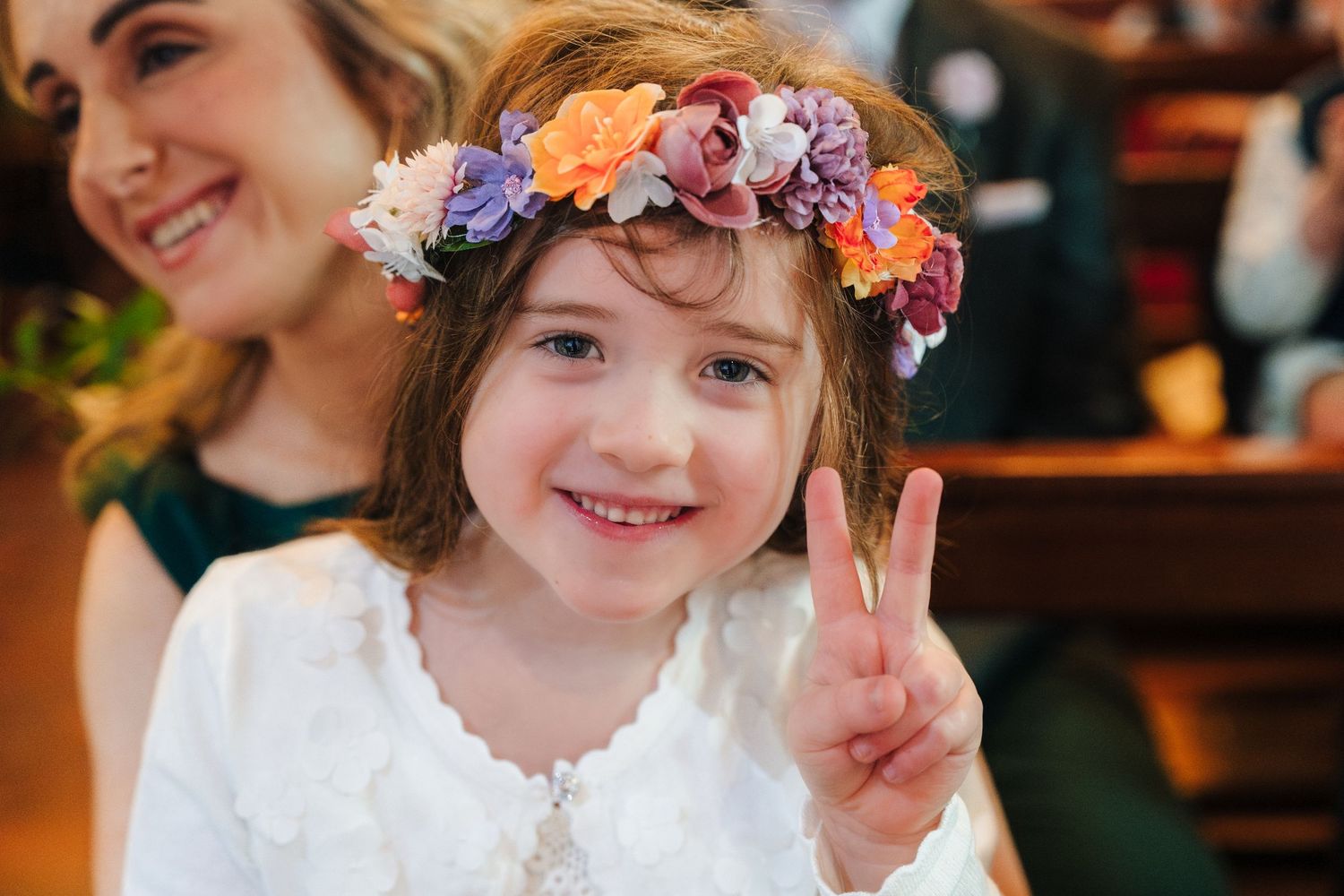 Young attendant wearing a floral crown and white dress smiles during wedding festivities.