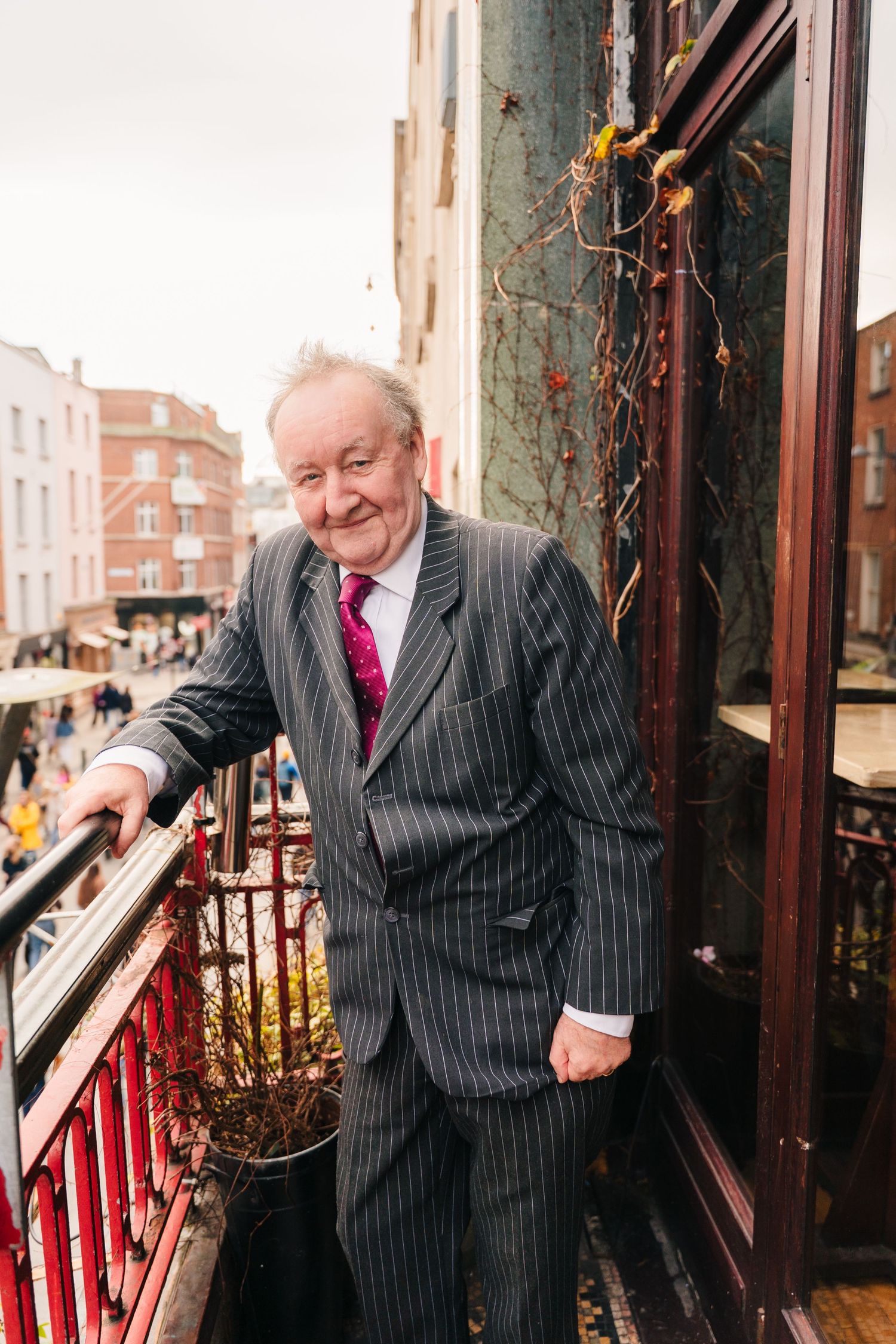 An elderly gentleman in a pinstriped suit stands on a balcony overlooking a city street. Dublin wedding photogrAPher Bewleys Grafton