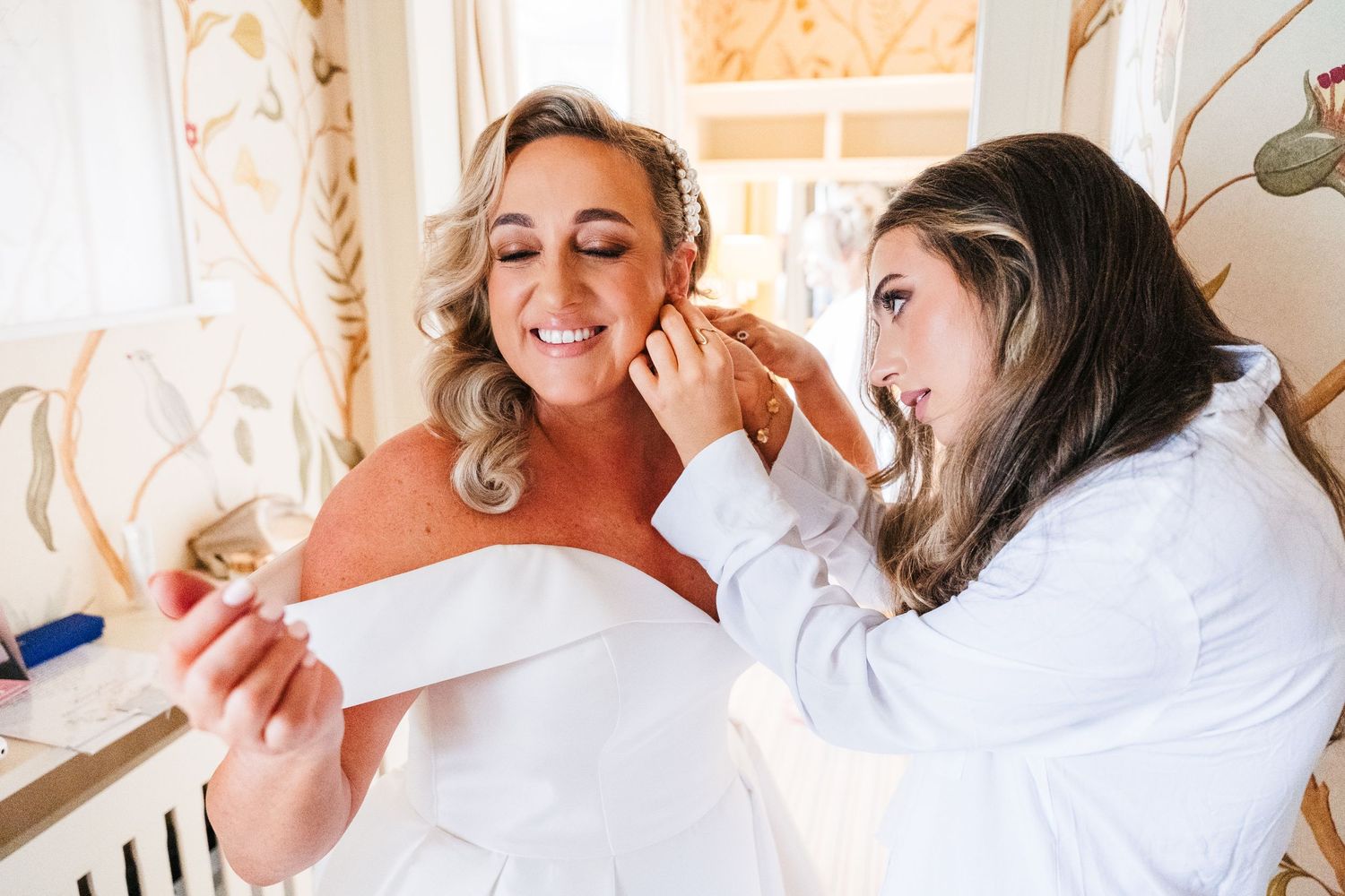 Two people getting ready in a bright room with white curtains and soft morning light. Virginia Park Lodge Wedding Photographer Dublin Meath